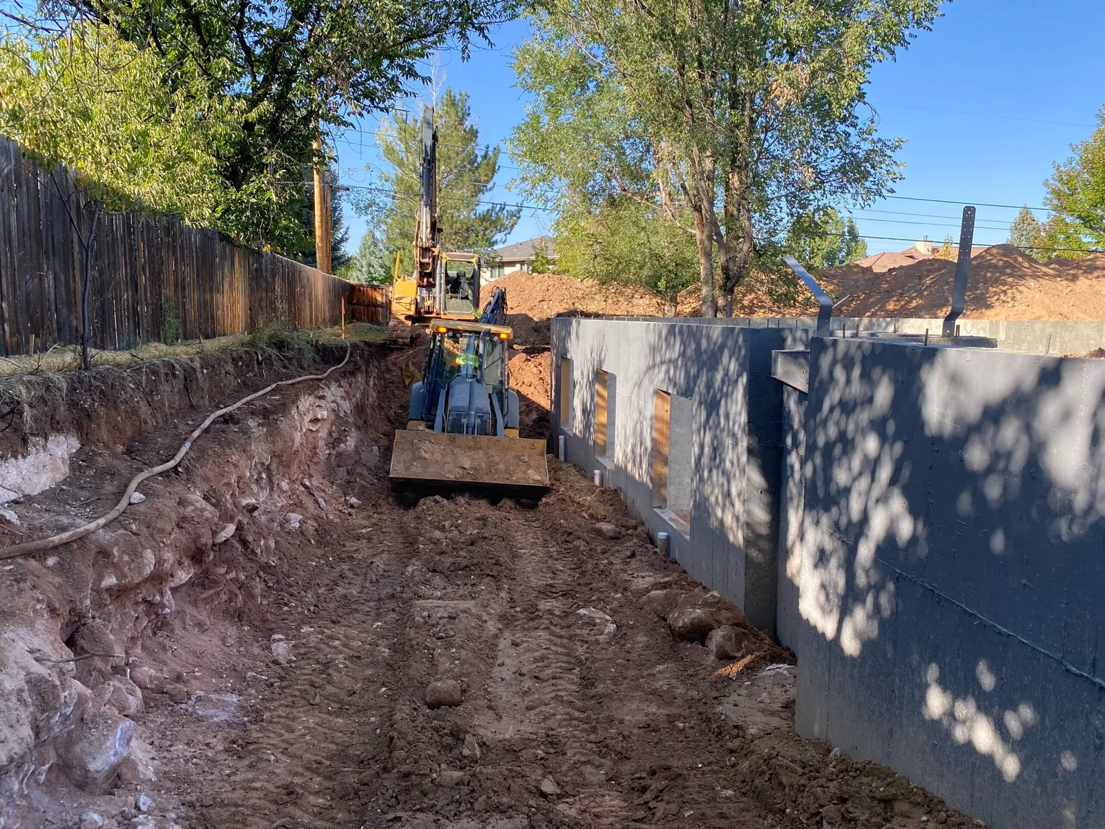 Backhoe working in the dig along new poured foundation walls with an excavator behind it
