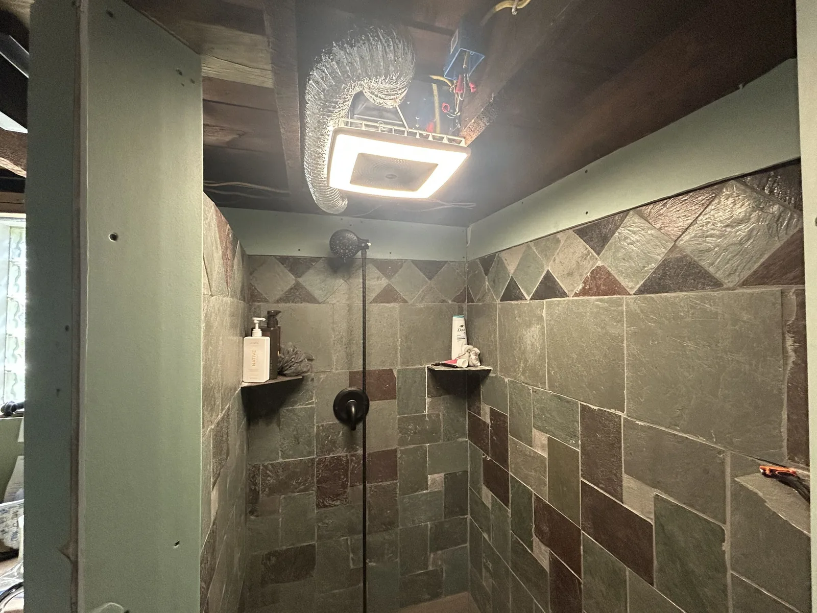 Tiled walk-in shower mid-remodel with new slate-look wall tile and a corner shelf