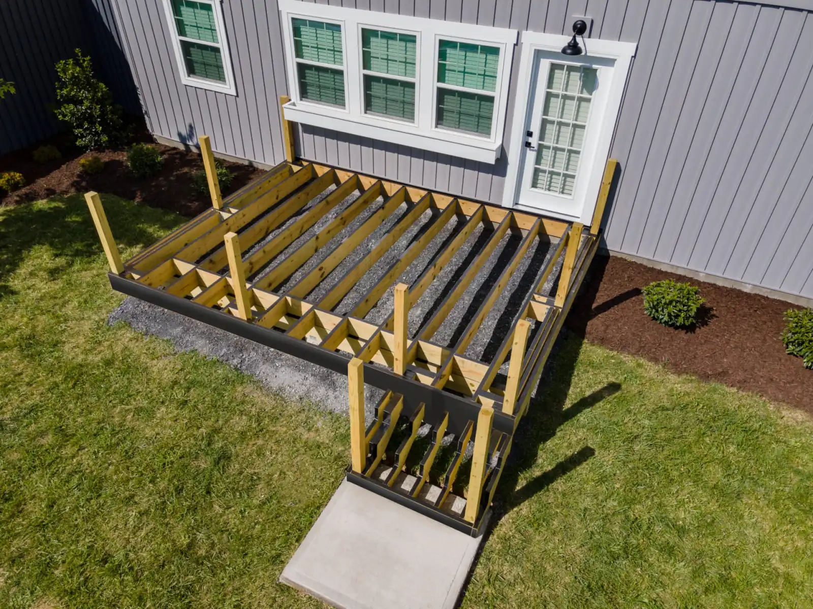New deck frame of joists, beams and posts built off the back of a house