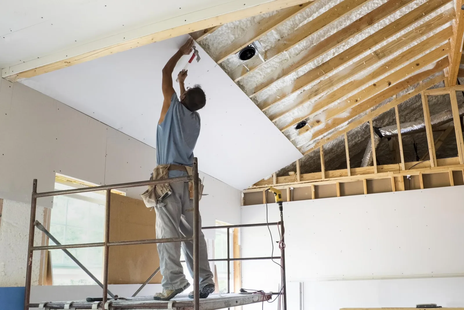 Worker on a scaffold hanging a drywall sheet on a vaulted ceiling