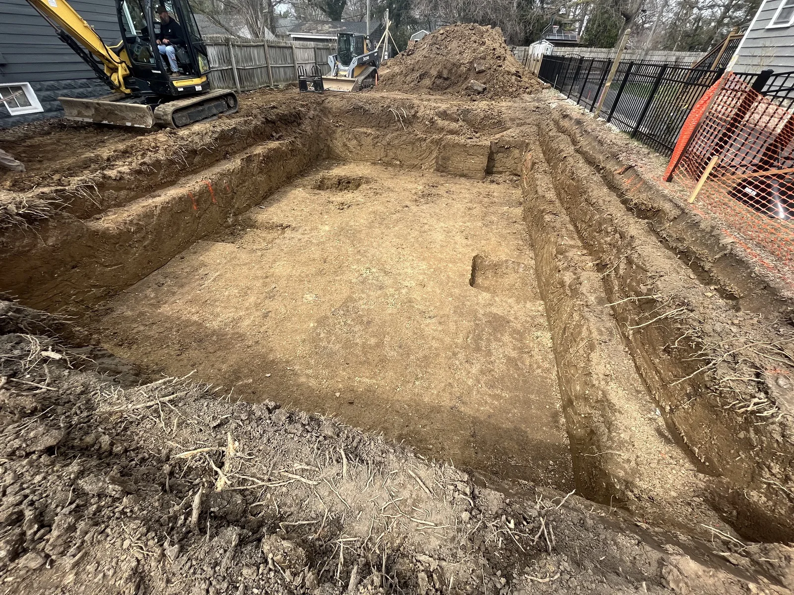 Mini excavator beside a freshly dug basement excavation on a residential lot