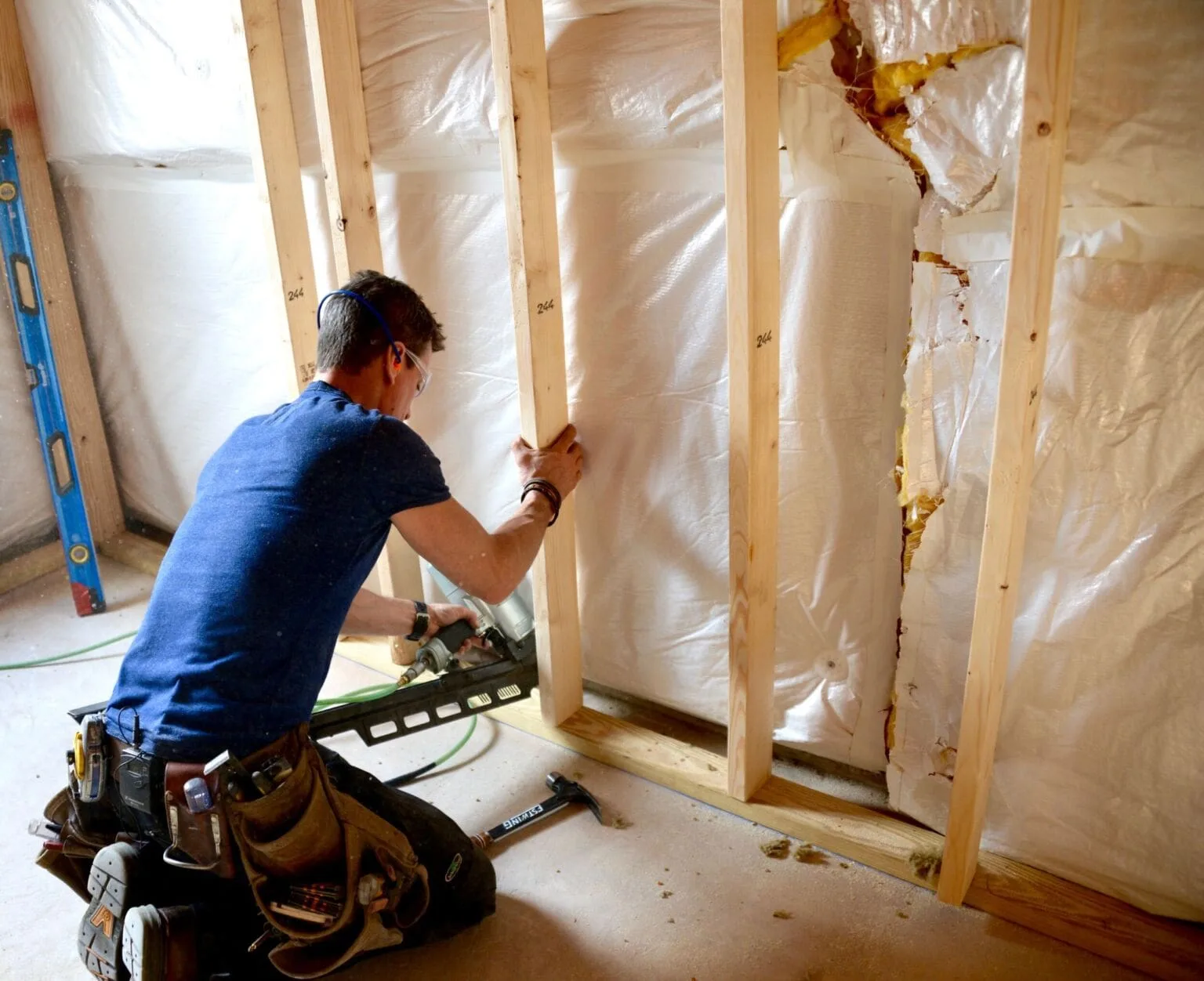 Carpenter kneeling with a nail gun fastening studs into a new wall