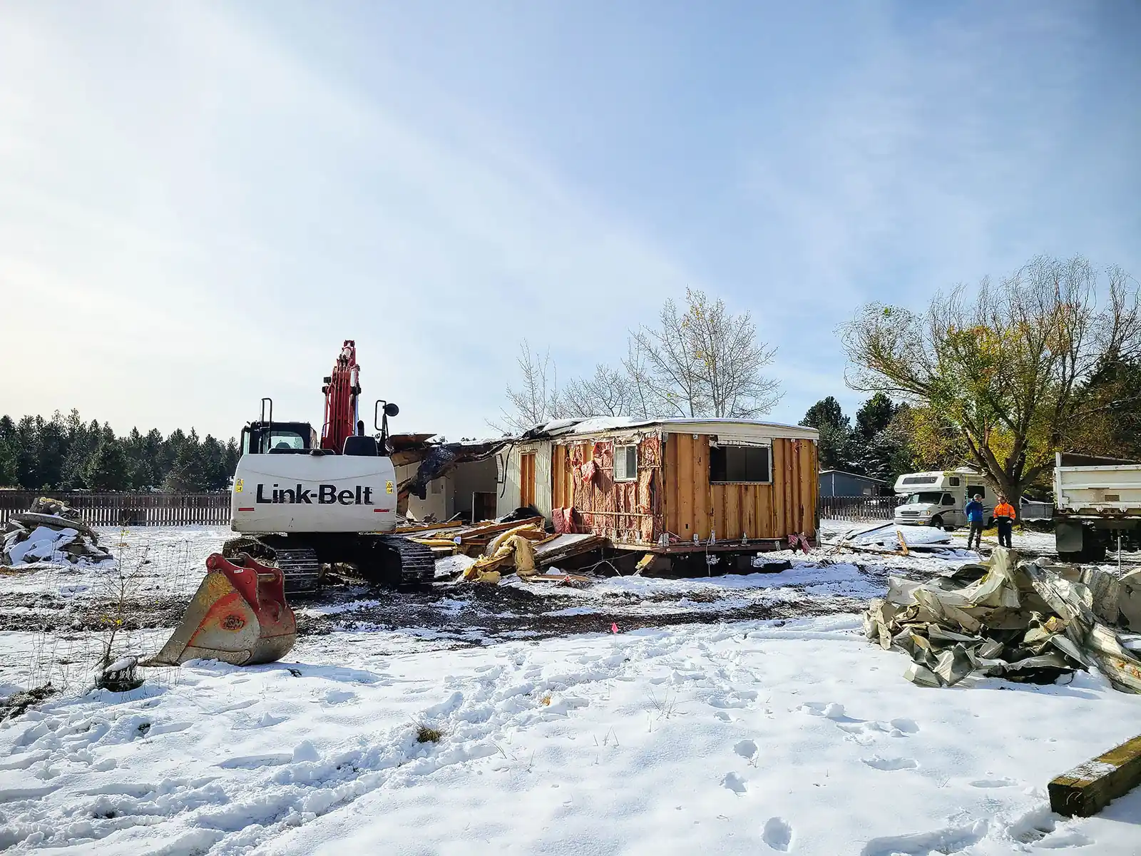 Small structure torn open to the framing with siding debris piled in snow