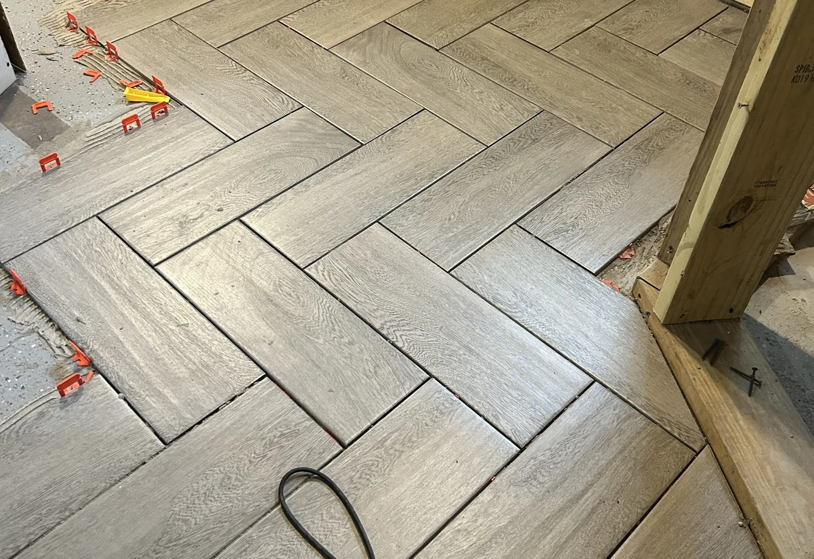 Close-up of herringbone plank tile with spacers set against a framed wall