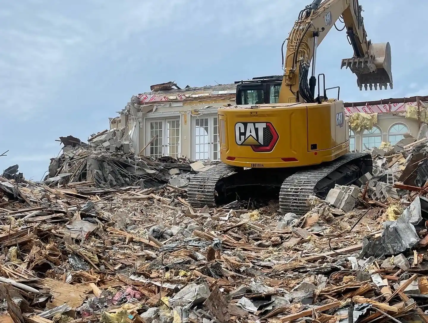 Excavator loading demolition debris from a torn-down house