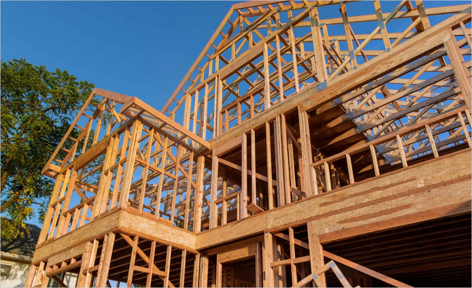 Two-story wood-framed house under construction against a clear sky