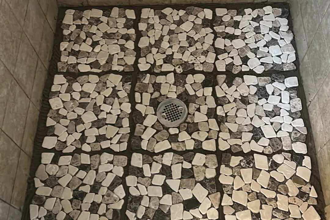 Pebble tile sheets set in thinset around a shower drain before grout