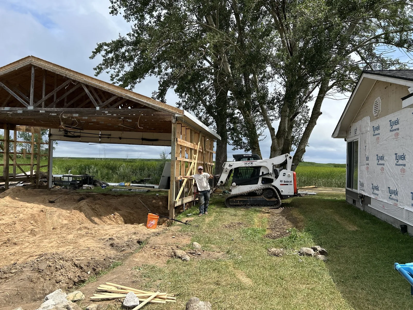 Post-frame building under construction with trusses set and a compact track loader on site