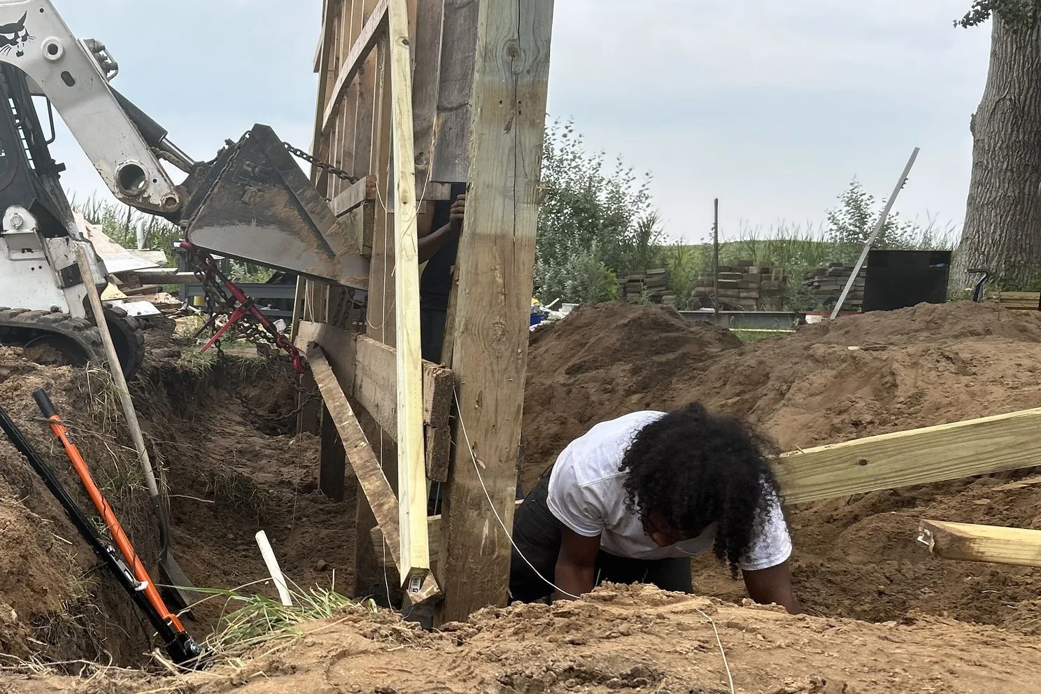 Crew member setting a treated post in a trench beside a compact track loader on a pole barn build